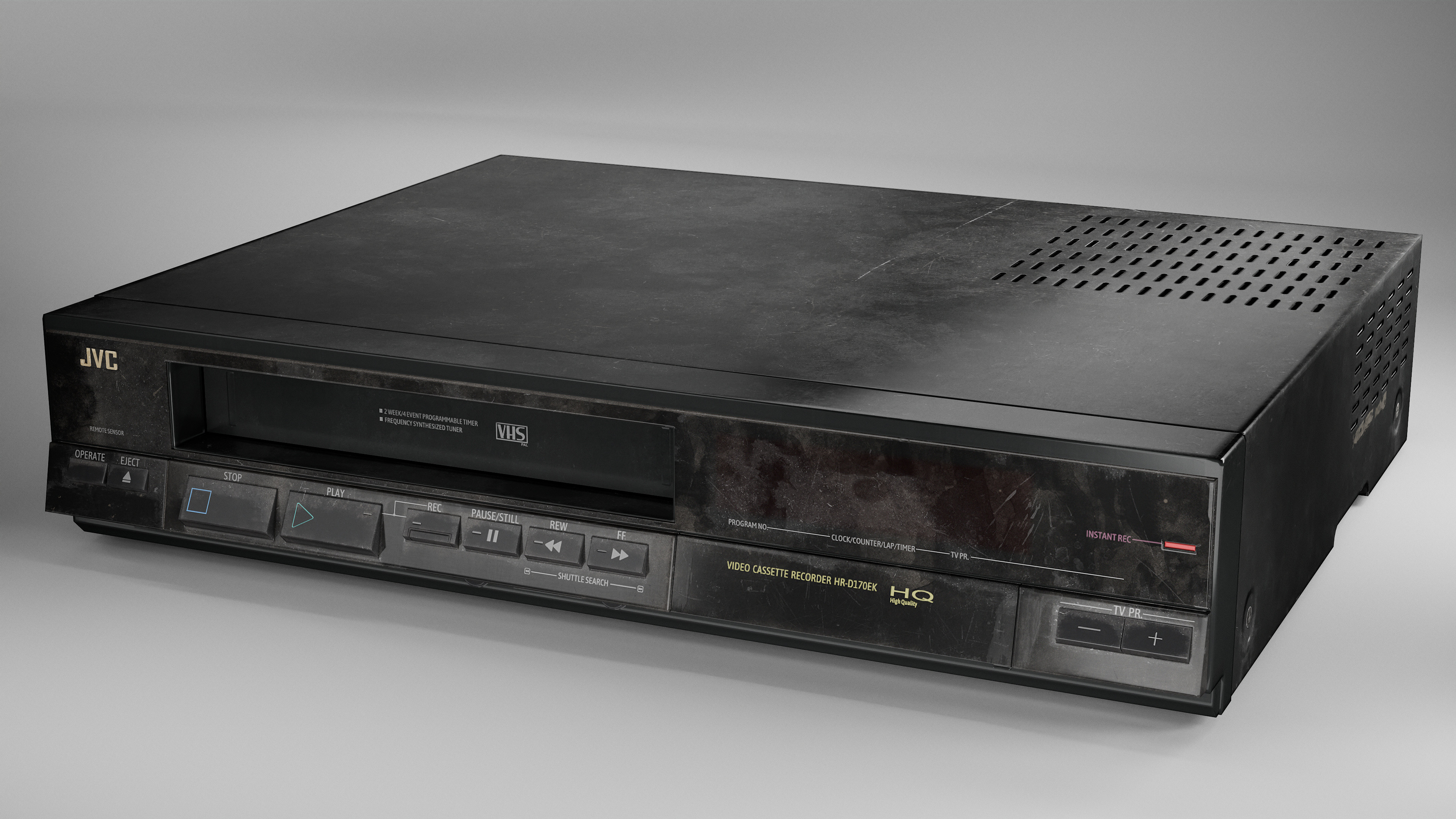 Black JVC VHS player with various buttons like play, stop, and eject. "Video Cassette Recorder" text visible. Set on a plain gray background.
